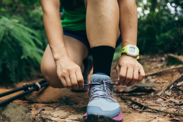 Woman ultra marathon runner tying shoelace on forest trail Woman ultra marathon runner tying shoelace on forest trail